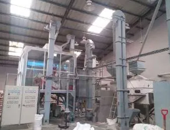 Ruang pabrik beratap rangka baja dengan rangkaian mesin bertingkat, menara elevator tegak, dan panel kontrol listrik; beberapa karung putih di lantai.