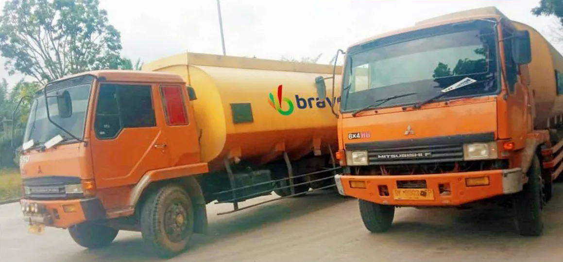 Dua truk tangki berkabin oranye terparkir berdampingan; salah satu tangki berlogo bravo.